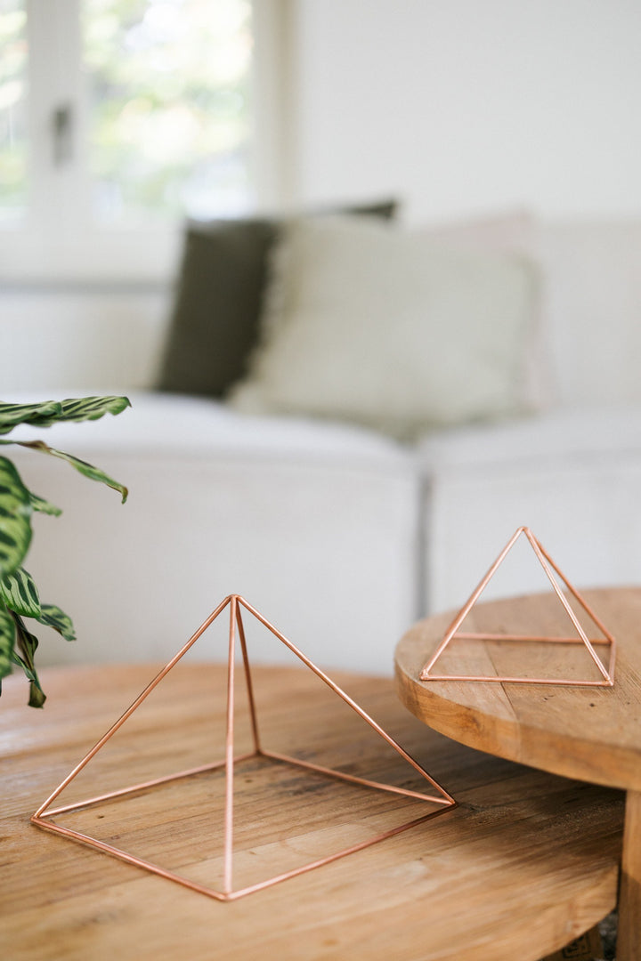 Kopero Pyramide énergisante en cuivre lisse, la petite et la grande pyramide côte à côte sur deux tables en bois
