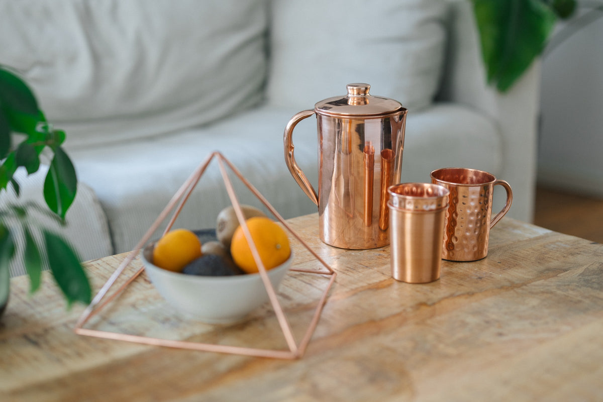 Pyramide en cuivre au-dessus d'une coupe de fruits, avec une cruche, un gobelet et un mug sur une table basse en bois