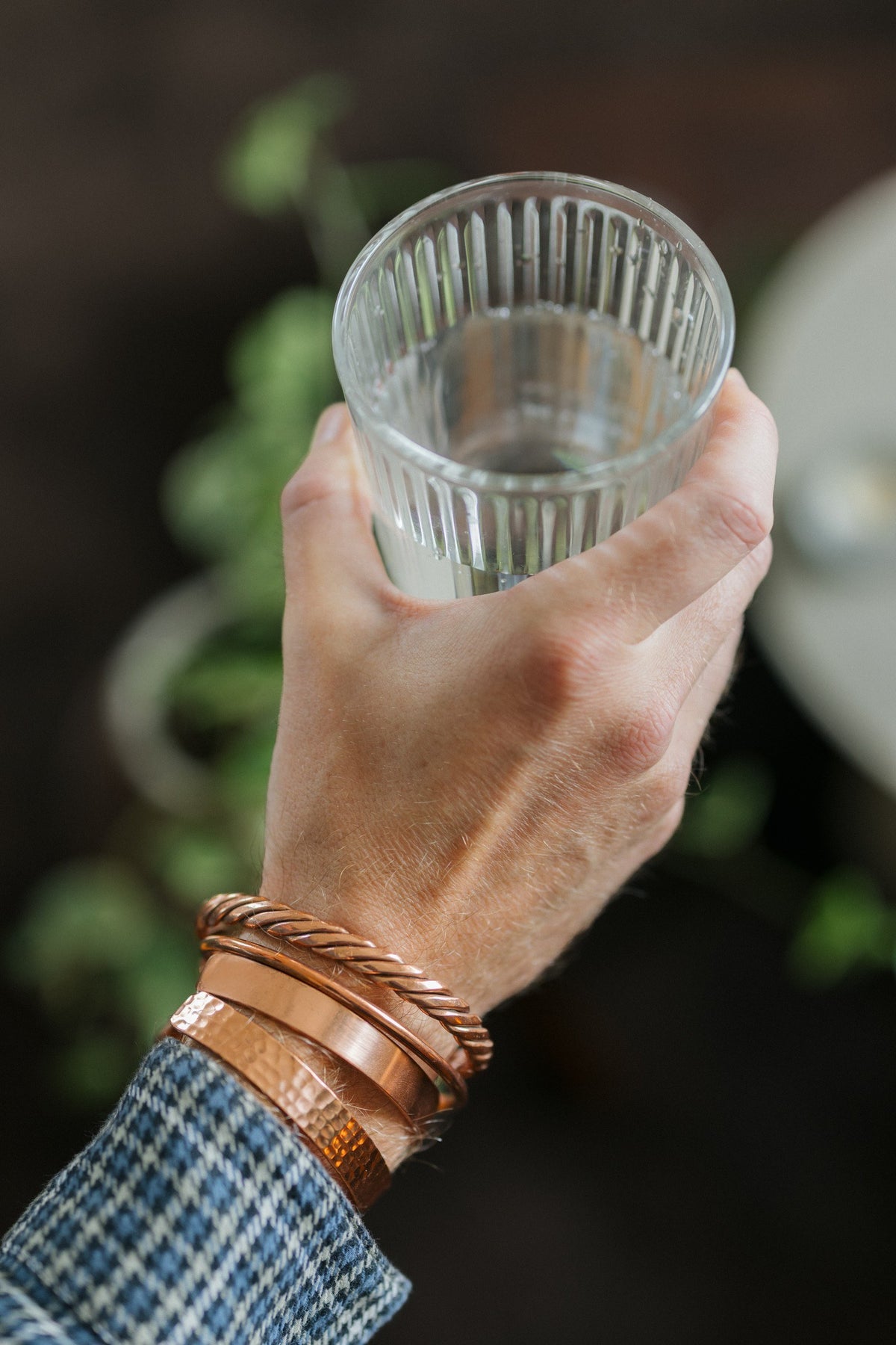 Kopero Bracelet en cuivre, les quatre versions ensemble à un seul poignet, avec un verre d'eau dans la main