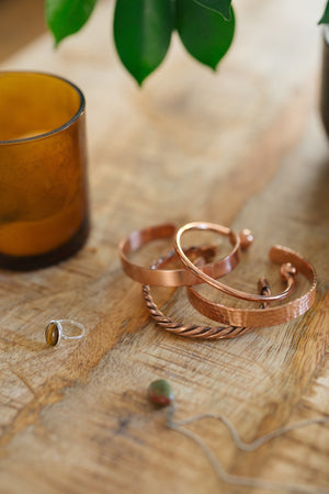 Kopero Bracelet en cuivre, les quatre versions ensemble sur une table en bois avec une bougie et une bague