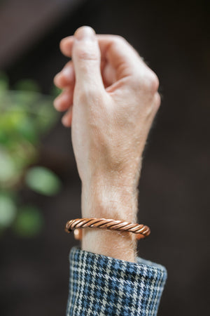 Kopero Bracelet en cuivre Torsadé, au poignet, avec la main levée devant un fond sombre
