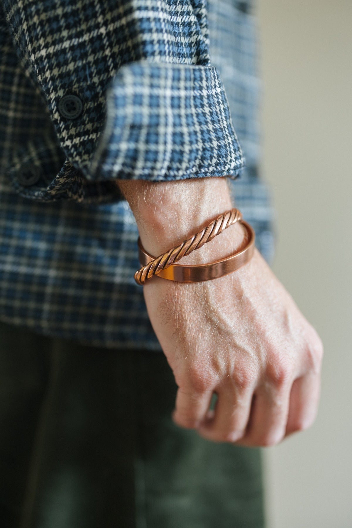 Kopero Bracelet en cuivre Torsadé, au poignet sur une manche de chemise à carreaux, avec un bracelet lisse