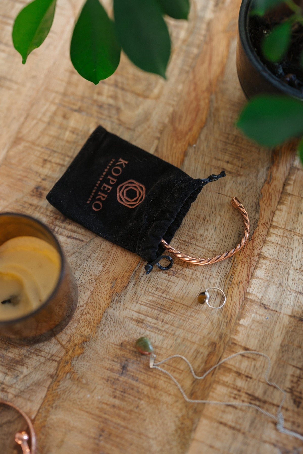 Kopero Bracelet en cuivre Torsadé, sur une table en bois à côté de la pochette en velours, d'une bougie et de bijoux