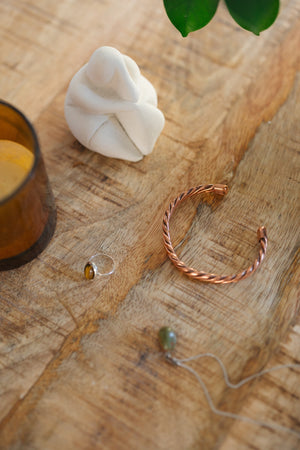 Kopero Bracelet en cuivre Torsadé, sur une table en bois à côté d'une figurine et d'une bague