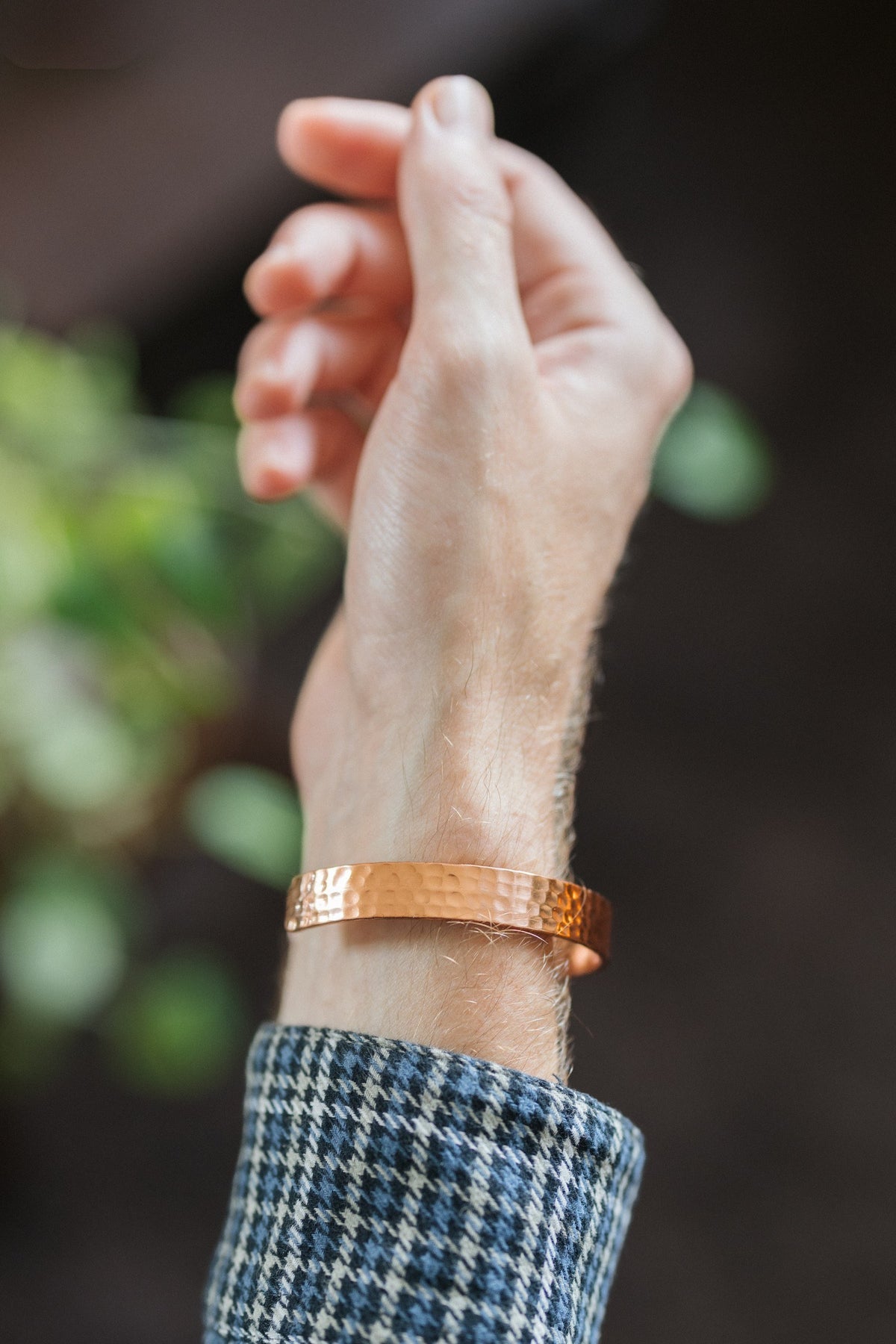 Kopero Bracelet en cuivre Martelé, au poignet, avec la main levée devant un fond sombre