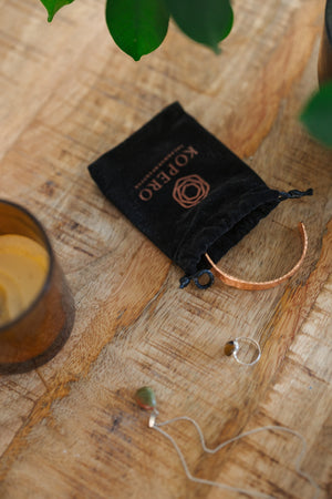 Kopero Bracelet en cuivre Martelé, sur une table en bois à côté de la pochette en velours, d'une bougie et de bijoux