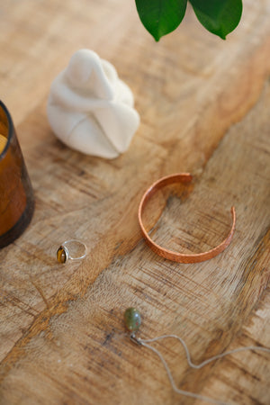 Kopero Bracelet en cuivre Martelé, sur une table en bois à côté d'une figurine et d'une bague