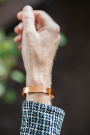 Kopero Bracelet en cuivre Lisse, au poignet, avec la main levée devant un fond sombre