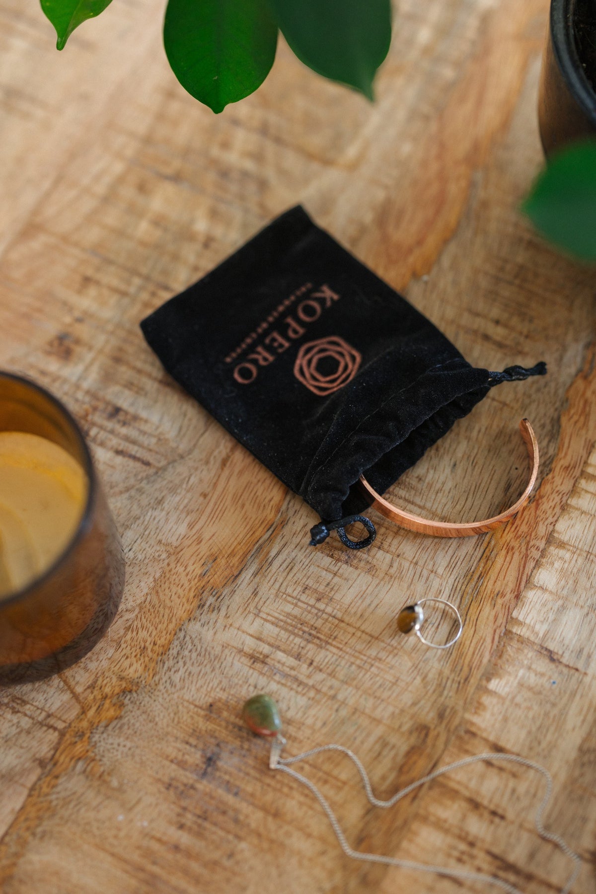 Kopero Bracelet en cuivre Lisse, sur une table en bois à côté de la pochette en velours, d'une bougie et de bijoux