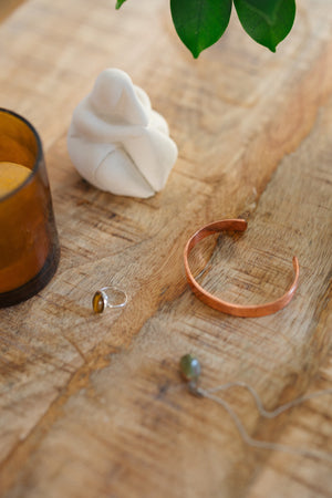 Kopero Bracelet en cuivre Lisse, sur une table en bois à côté d'une figurine et d'une bague