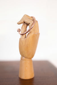 Bracelet en cuivre rond Kopero sur une main à bijoux en bois