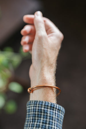 Kopero Bracelet en cuivre Rond, au poignet, avec la main levée devant un fond sombre