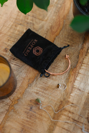 Kopero Bracelet en cuivre Rond, sur une table en bois à côté de la pochette en velours, d'une bougie et de bijoux