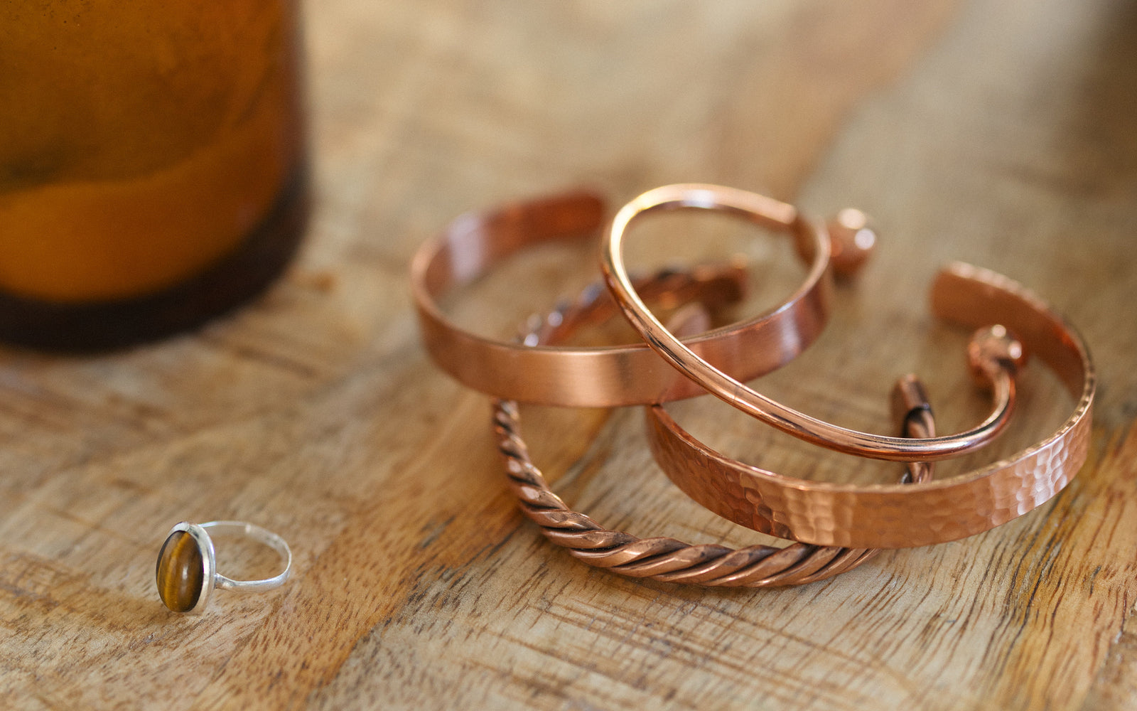 Quatre bracelets en cuivre, torsadé, lisse, martelé et rond, sur une table en bois à côté d'une bougie et d'une bague