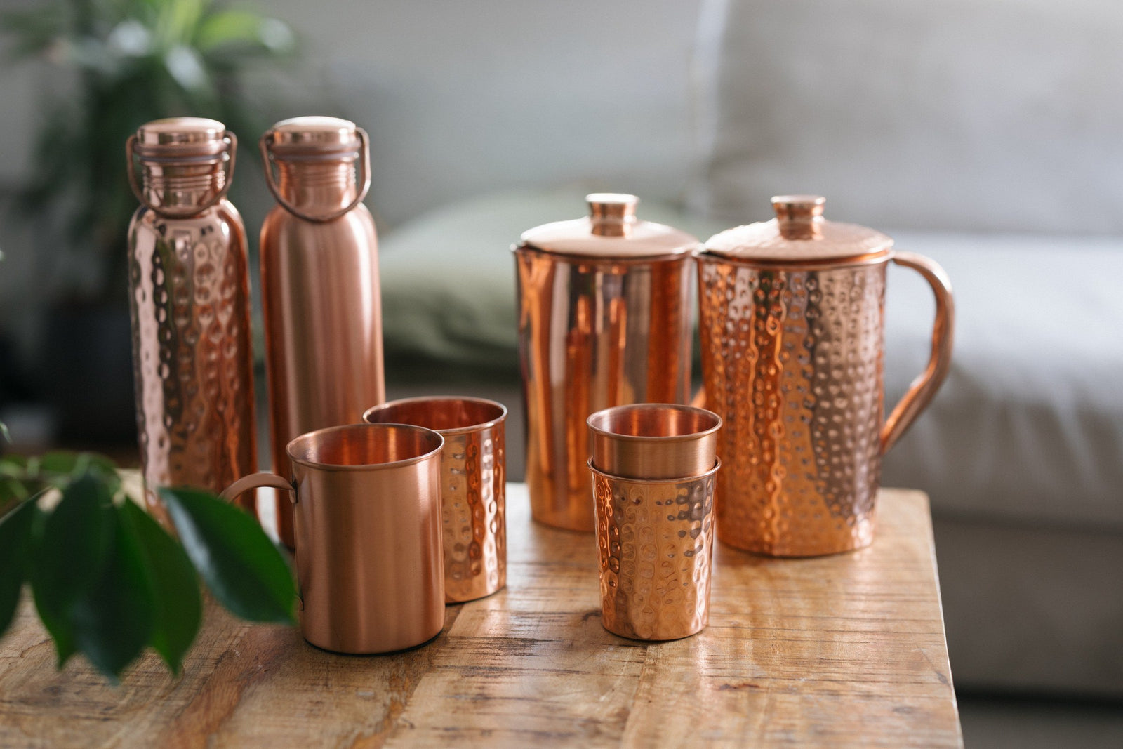 Gourdes, cruches, mugs et gobelets en cuivre sur une table en bois devant un canapé