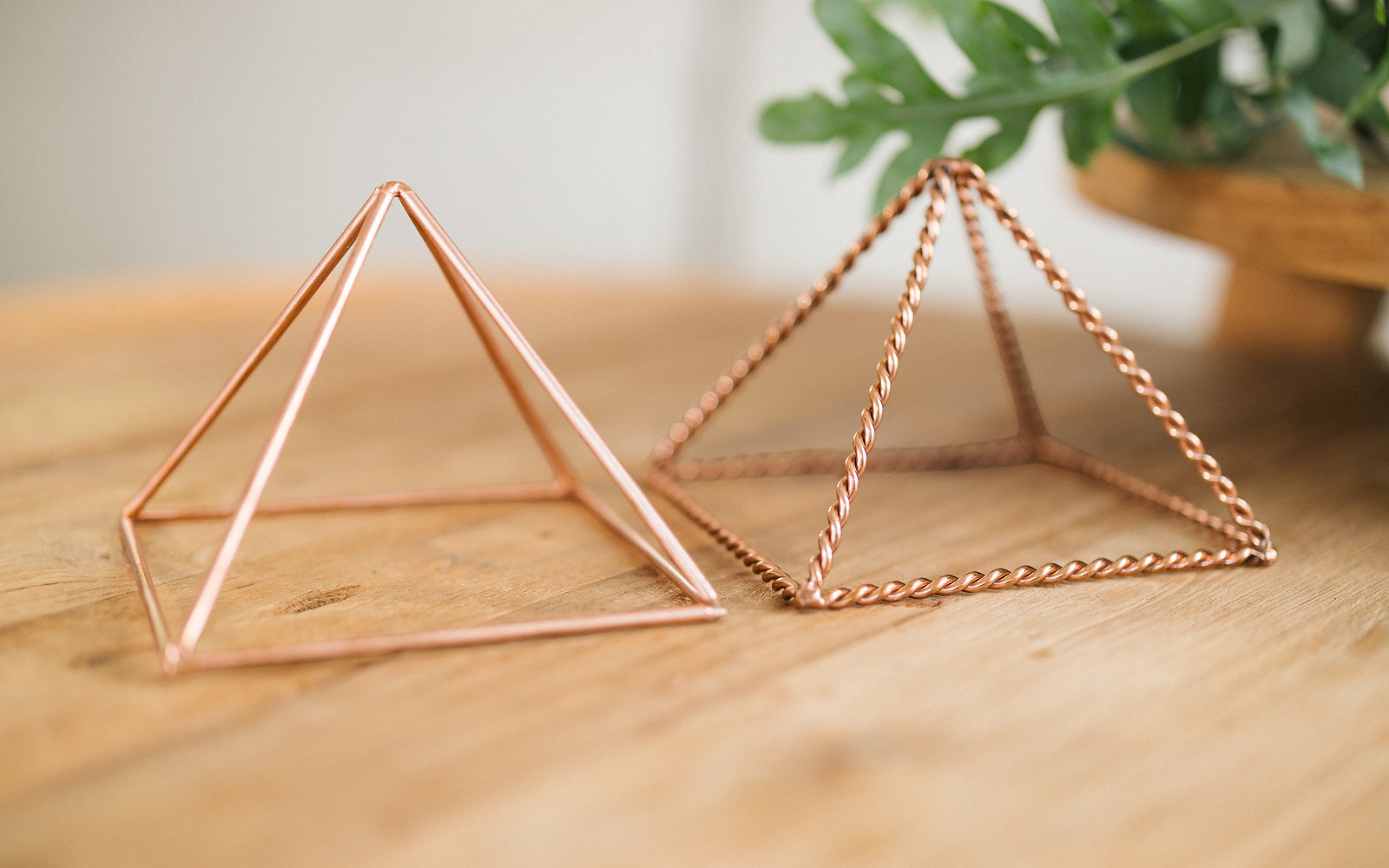 Deux pyramides en cuivre, torsadée et lisse, côte à côte sur une table en bois