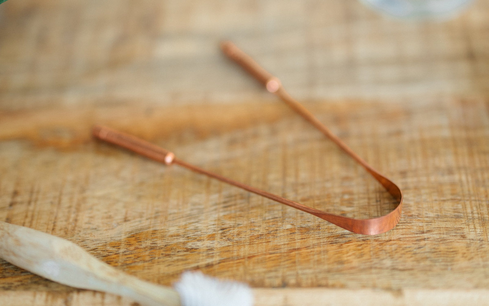 Gratte-langue en cuivre sur une table en bois, à côté d'une brosse à dents en bambou