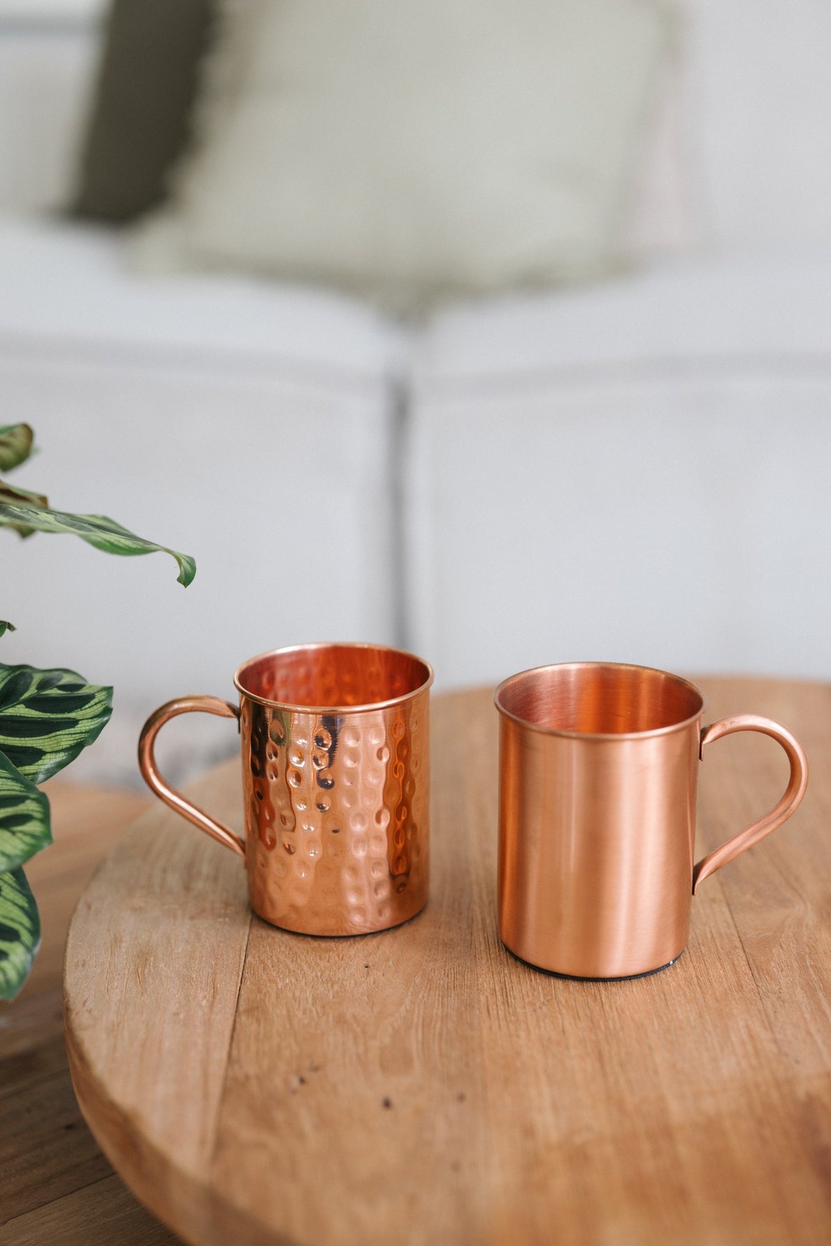 Kopero Mug en cuivre, un mug lisse et un mug martelé côte à côte sur une table ronde en bois