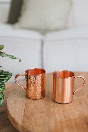 Kopero Mug en cuivre, un mug lisse et un mug martelé côte à côte sur une table ronde en bois
