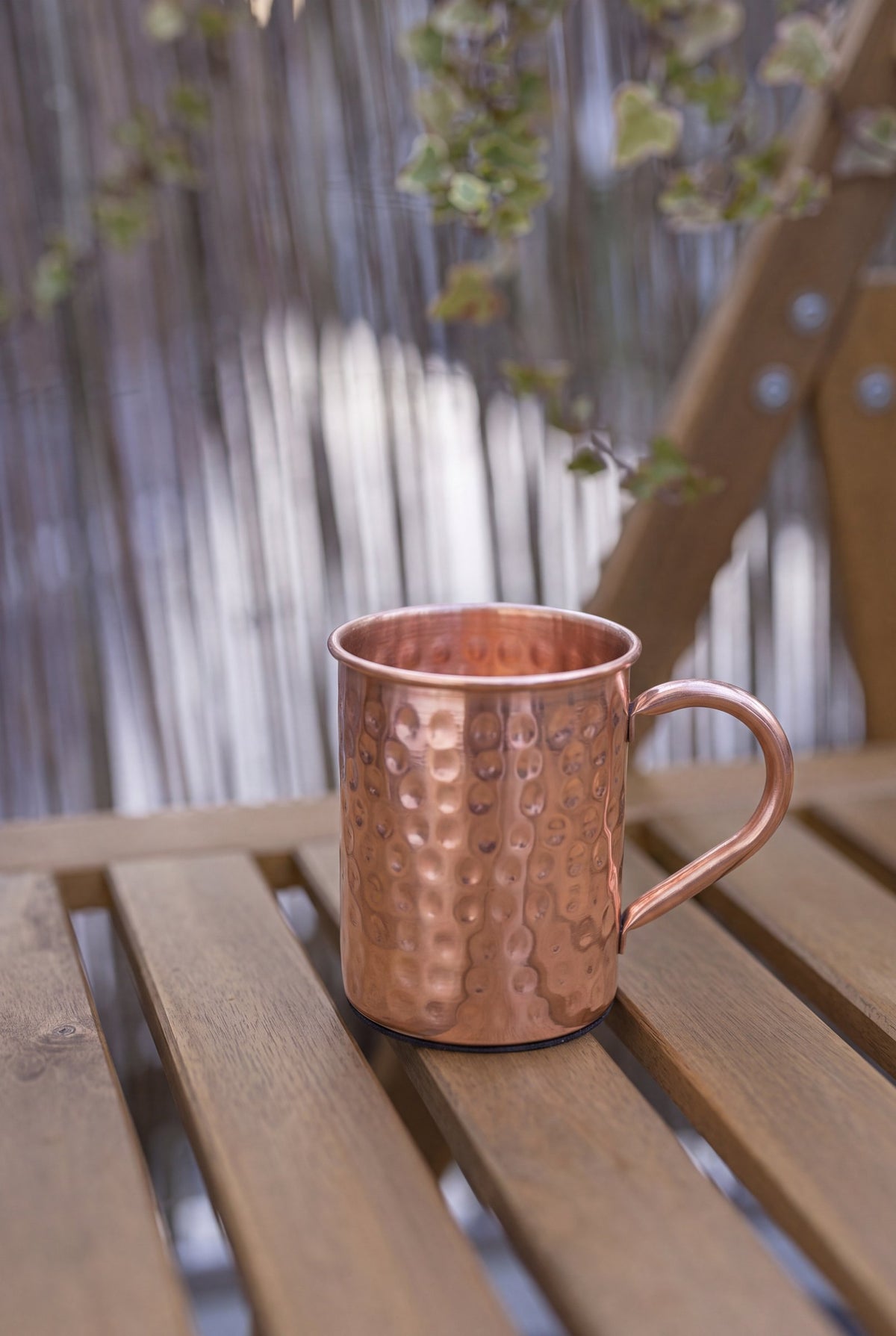 Mug en cuivre Kopero Martelé de 400 ml sur un banc de jardin en bois