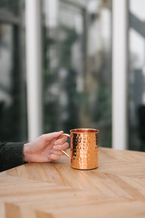 Kopero Mug en cuivre Martelé, sur une table en bois, avec une main sur l'anse