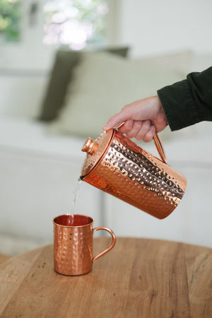 Kopero Mug en cuivre Martelé, pendant que de l'eau y est versée depuis une cruche en cuivre