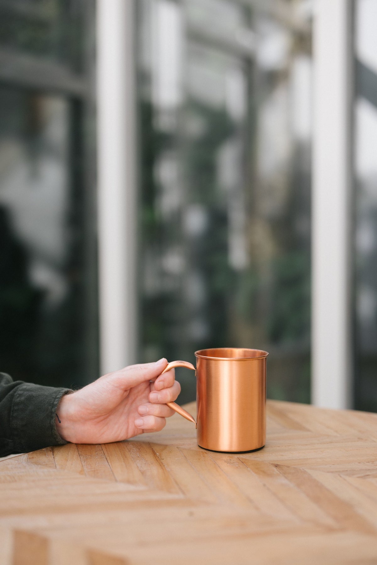 Kopero Mug en cuivre Lisse, sur une table en bois, avec une main sur l'anse