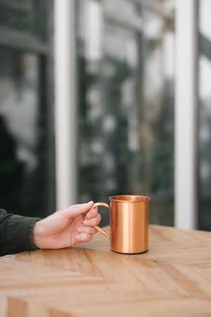 Kopero Mug en cuivre Lisse, sur une table en bois, avec une main sur l'anse
