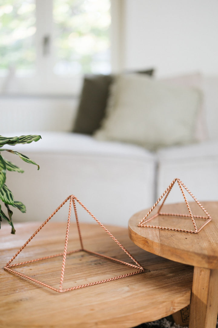 Kopero Pyramide énergisante en cuivre torsadé, la petite et la grande pyramide côte à côte sur deux tables en bois
