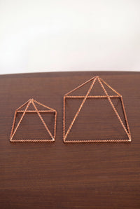 Pyramide énergisante en cuivre torsadé Kopero, les deux tailles côte à côte sur une table en bois