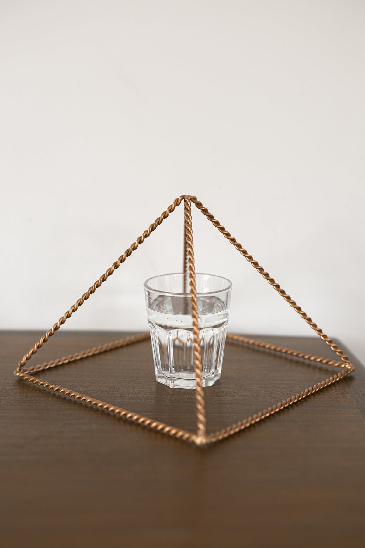 Pyramide énergisante en cuivre torsadé Kopero Grande (23,56 cm) au-dessus d'un verre d'eau