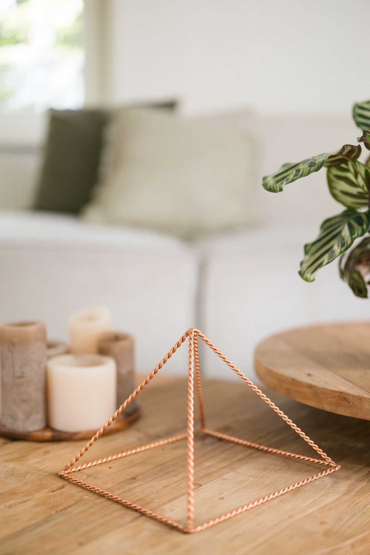 Kopero Pyramide énergisante en cuivre torsadé Grande (23,56 cm), sur une table basse en bois devant un canapé, à côté de bougies