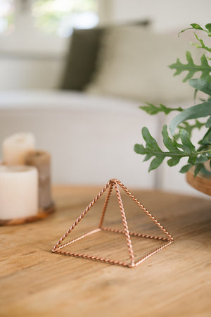 Kopero Pyramide énergisante en cuivre torsadé Petite (14,56 cm), sur une table en bois à côté de bougies