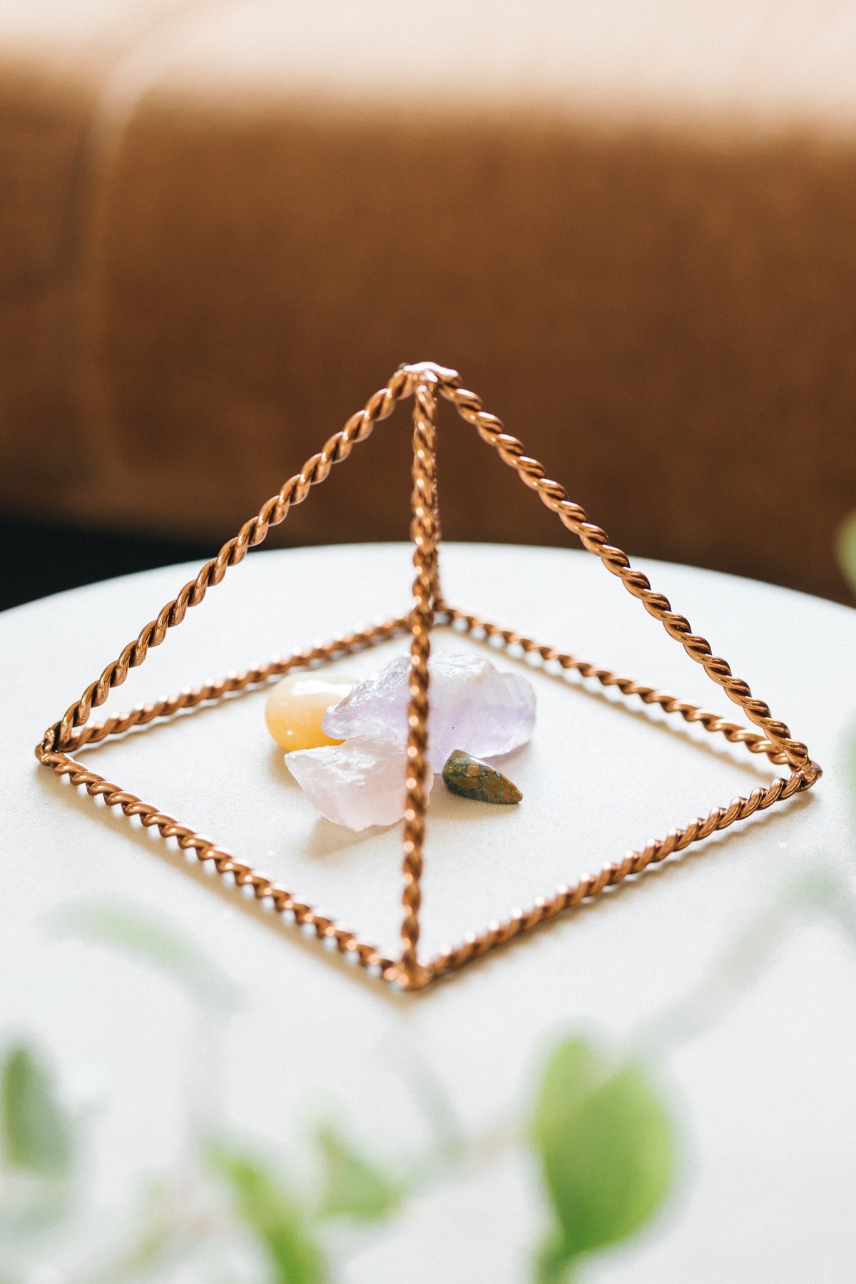 Kopero Pyramide énergisante en cuivre torsadé Petite (14,56 cm), avec des pierres précieuses dessous sur une petite table blanche