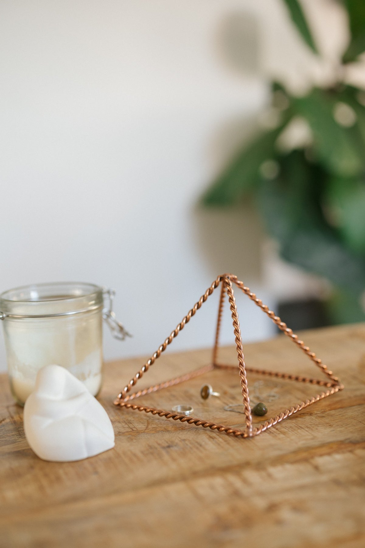 Kopero Pyramide énergisante en cuivre torsadé Petite (14,56 cm), avec des bijoux dessous à côté d'un pot de bougie et d'une figurine