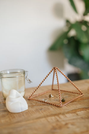 Kopero Pyramide énergisante en cuivre torsadé Petite (14,56 cm), avec des bijoux dessous à côté d'un pot de bougie et d'une figurine