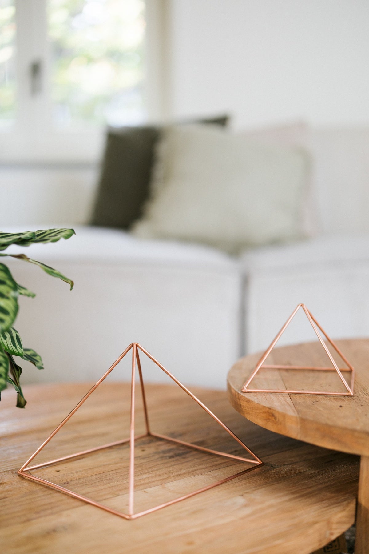 Kopero Pyramide énergisante en cuivre lisse, la petite et la grande pyramide côte à côte sur deux tables en bois