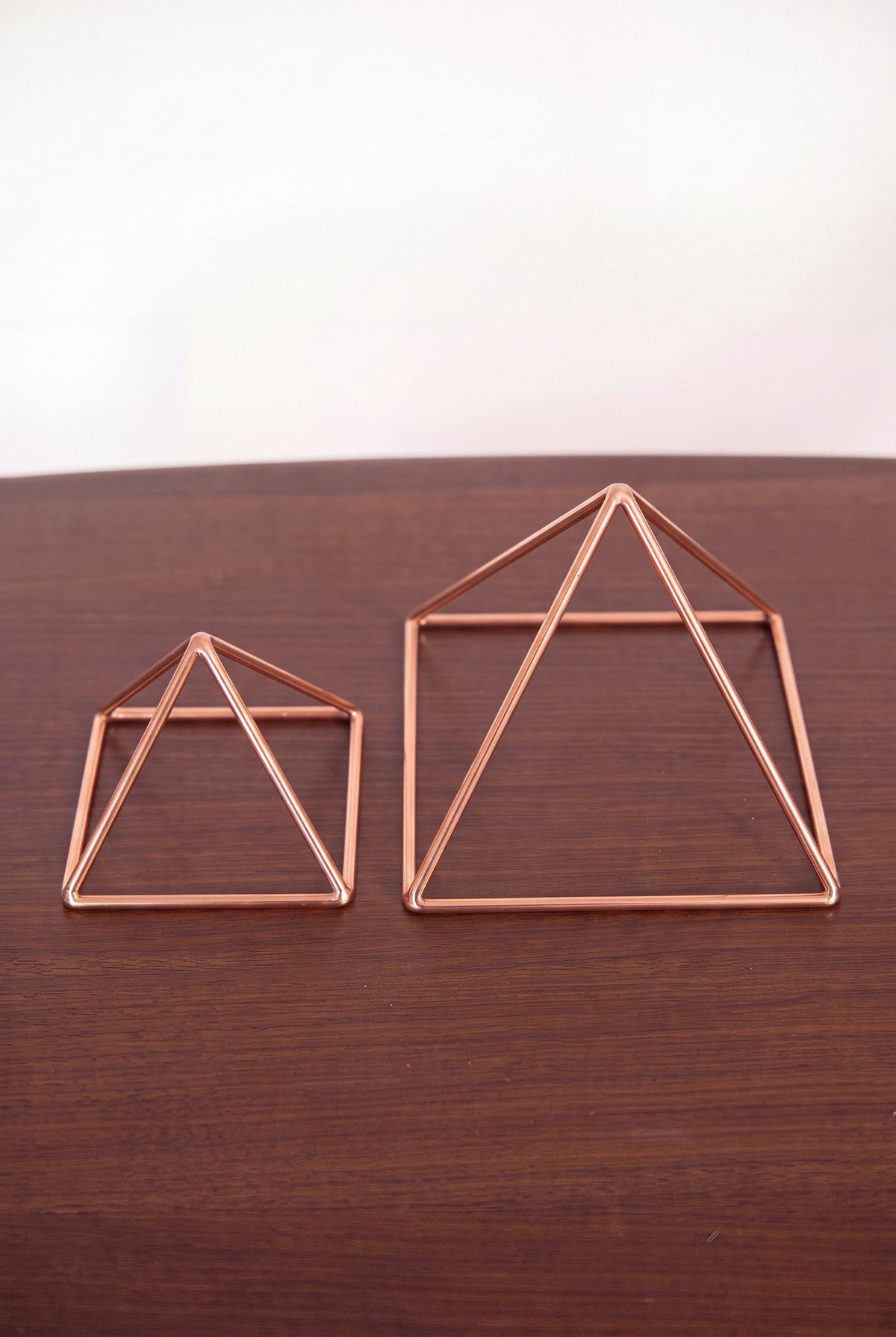 Pyramide énergisante en cuivre lisse Kopero, les deux tailles côte à côte sur une table en bois