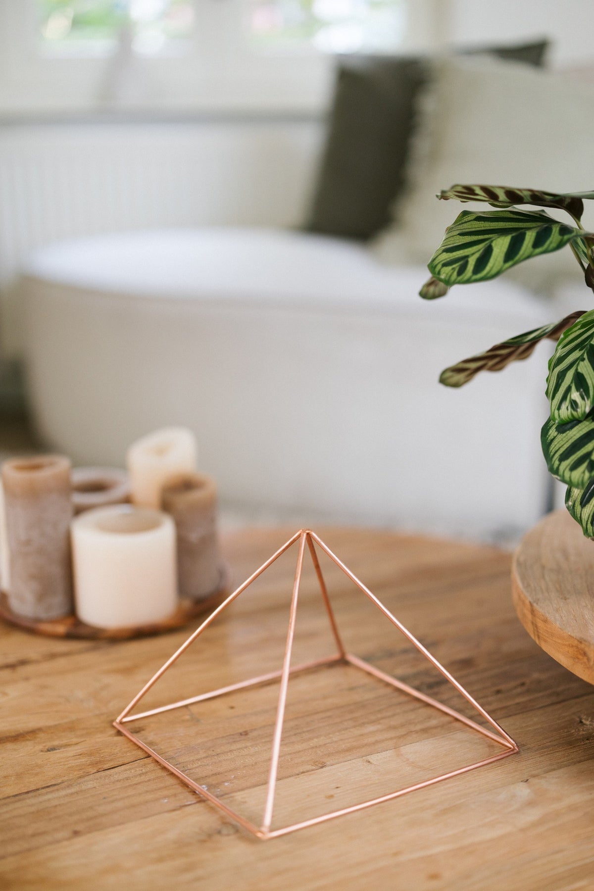 Kopero Pyramide énergisante en cuivre lisse Grande (23,56 cm), sur une table basse en bois devant un canapé, à côté de bougies