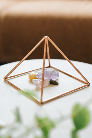 Kopero Pyramide énergisante en cuivre lisse Petite (14,56 cm), avec des pierres précieuses dessous sur une petite table blanche