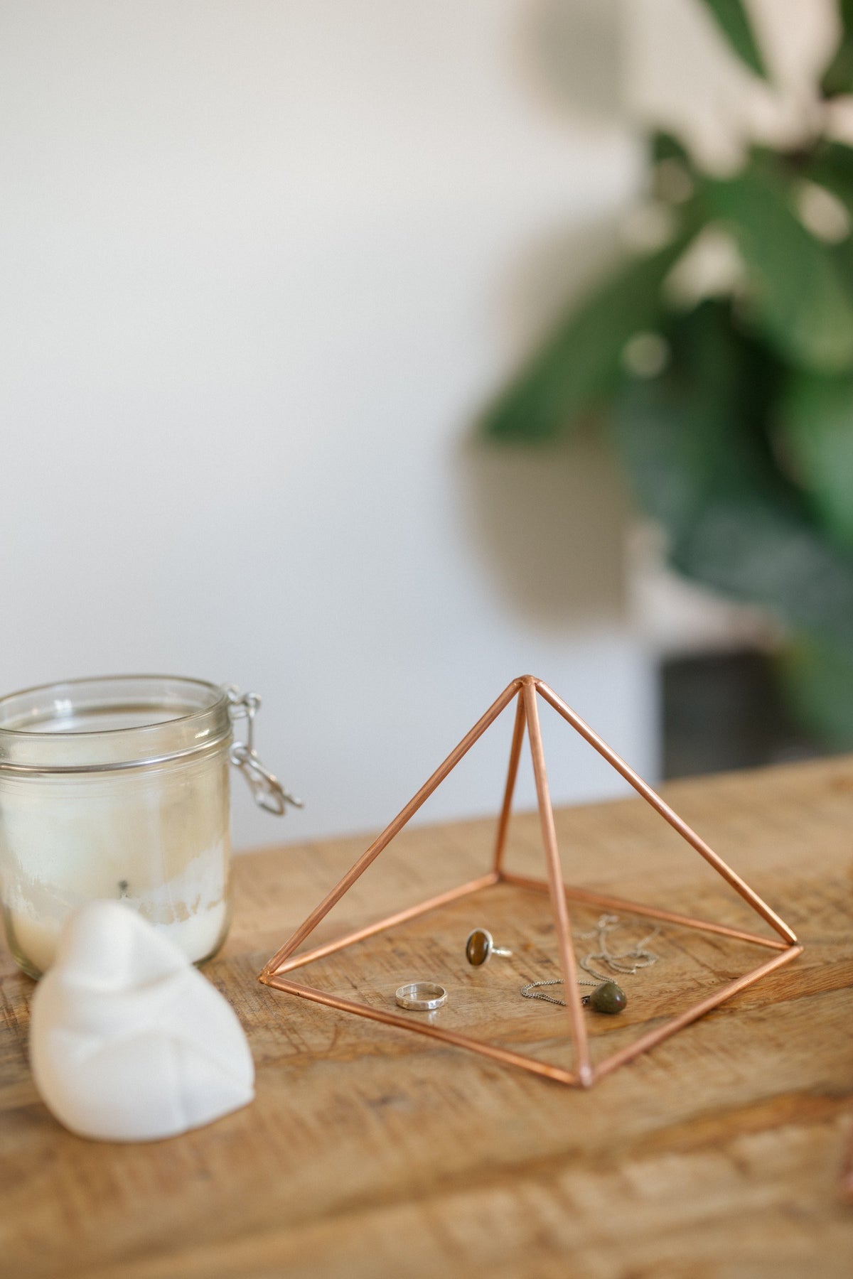 Kopero Pyramide énergisante en cuivre lisse Petite (14,56 cm), avec des bijoux dessous à côté d'un pot de bougie et d'une figurine
