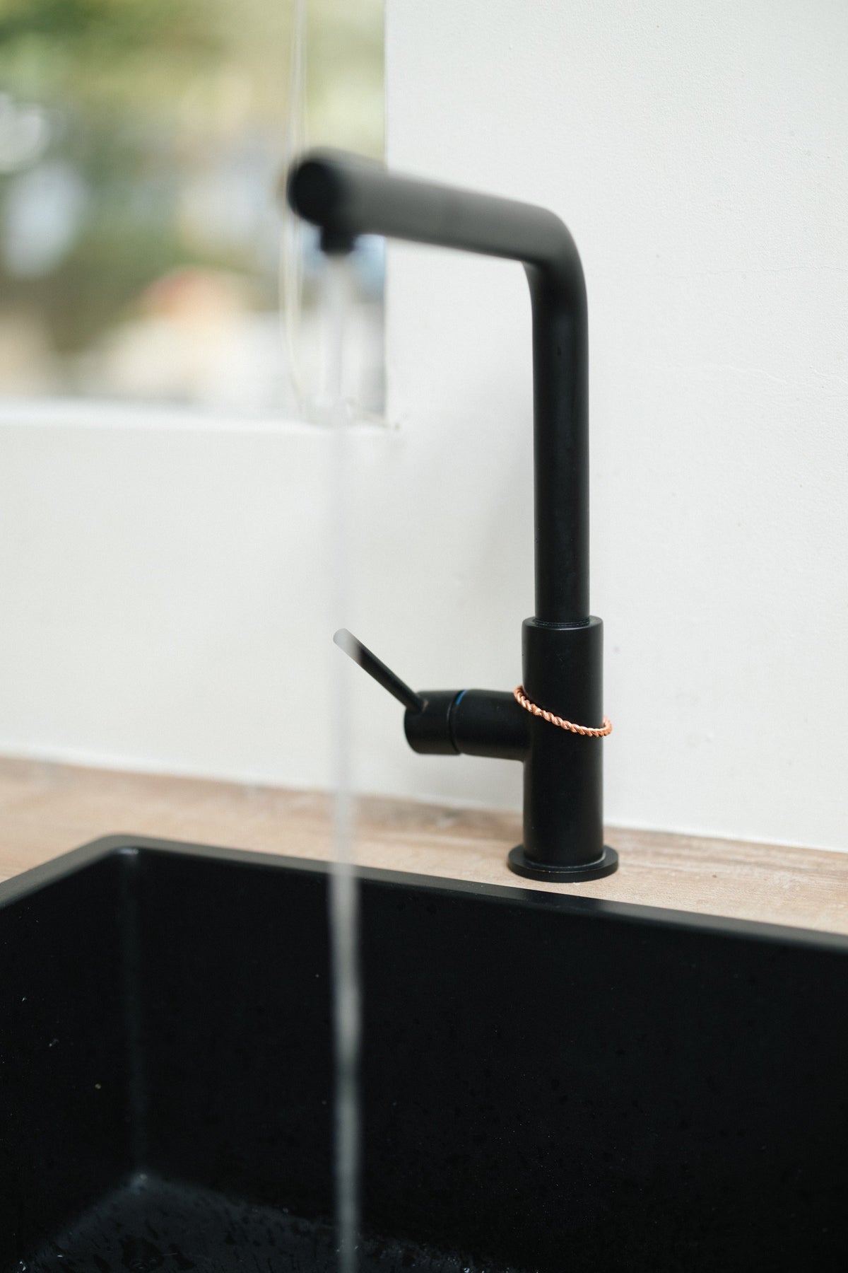 Kopero Anneau tenseur en cuivre, autour du robinet d'une robinetterie de cuisine noire avec de l'eau qui coule