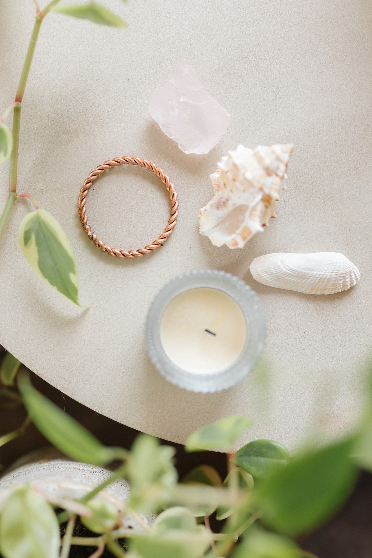 Kopero Anneau tenseur en cuivre, sur une petite table crème à côté d'un quartz rose, d'un coquillage et d'une bougie chauffe-plat