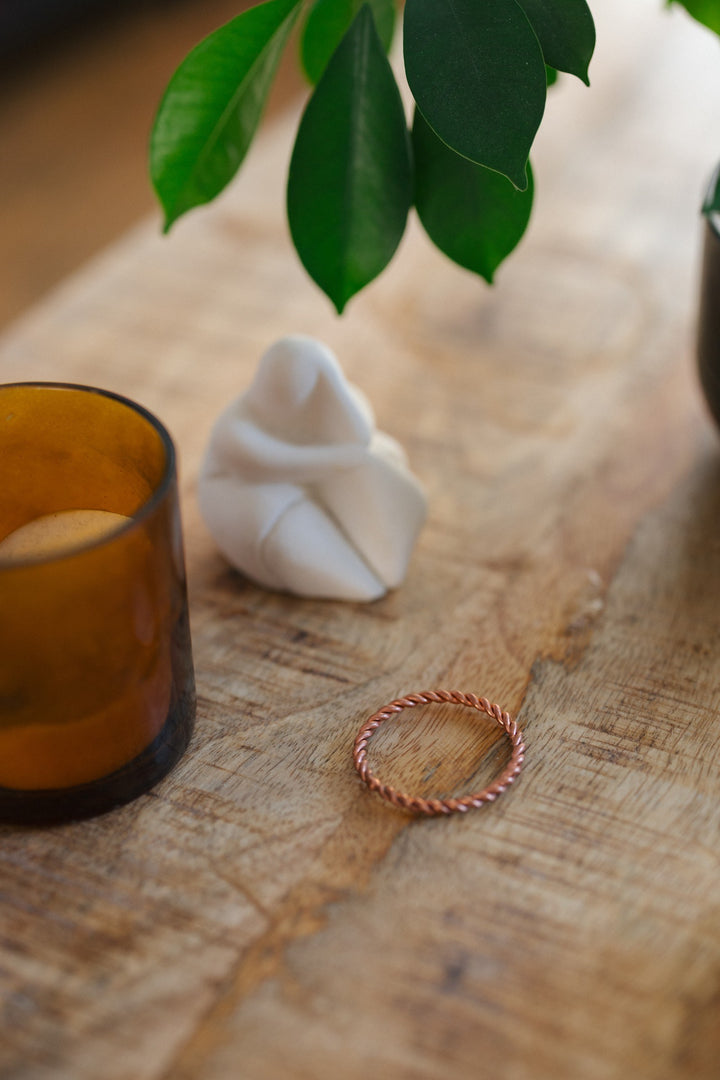 Kopero Anneau tenseur en cuivre, sur une table en bois à côté d'un bougeoir en verre et d'une figurine