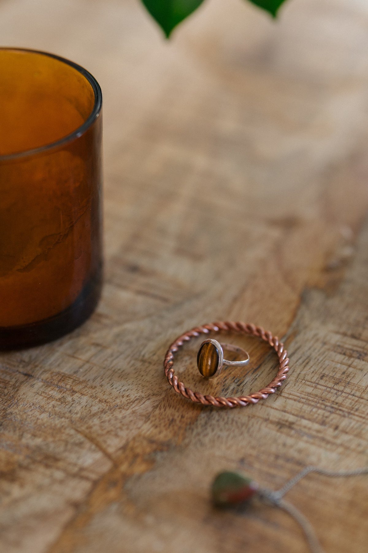 Kopero Anneau tenseur en cuivre, sur une table en bois avec une bague en œil-de-tigre et un bougeoir en verre