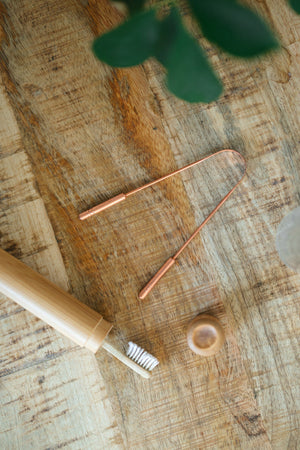 Kopero Gratte-langue en cuivre, sur une planche en bois à côté d'une brosse à dents en bambou