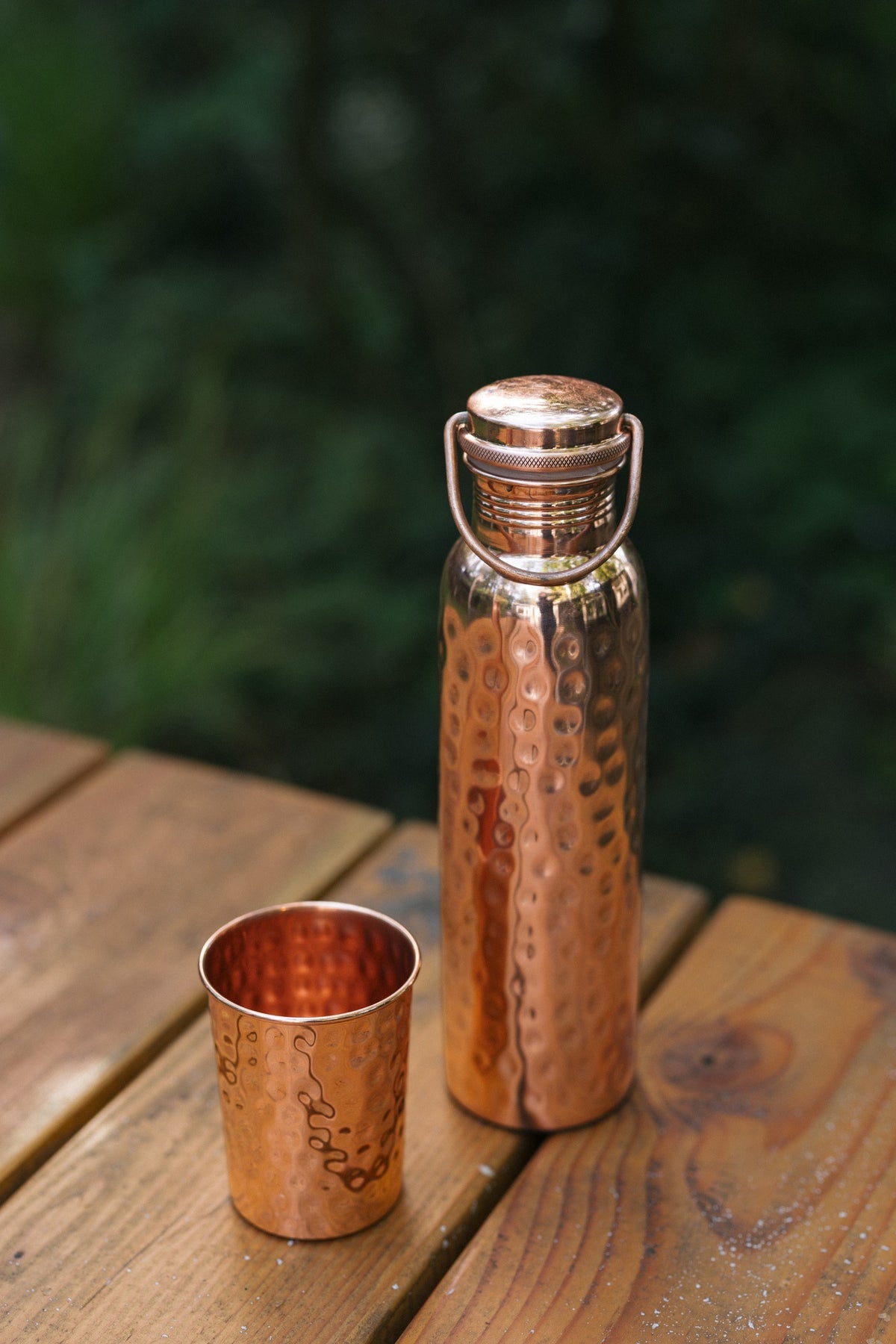 Kopero Gourde en cuivre Martelé, sur une table de jardin en bois à côté d'un gobelet martelé